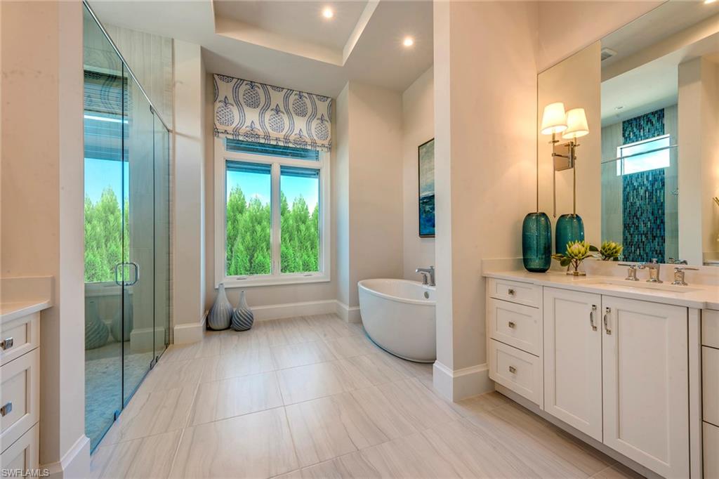 9828 Montiano Place Naples, FL 34113 - Photo 25 of 30 a spacious bathroom with a double vanity sink a large mirror a bathtub and next to a window