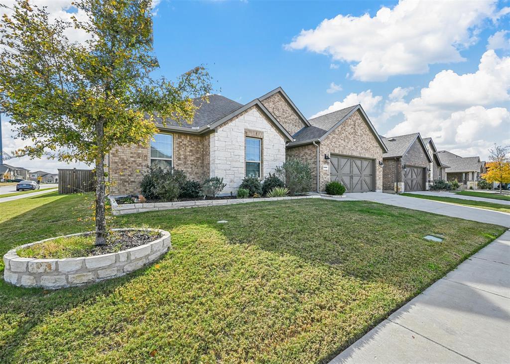 View of front of house with driveway, brick siding, a front yard, a shingled roof, and stone siding