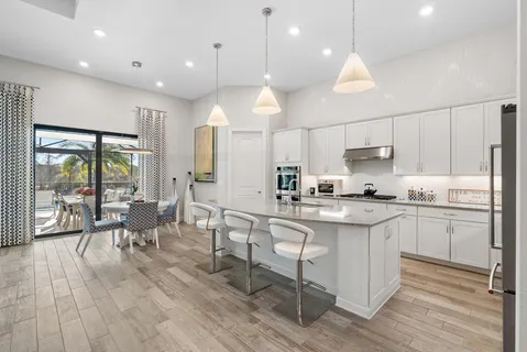 a kitchen with stainless steel appliances a dining table chairs stove and white cabinets next to a large window
