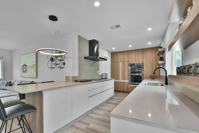 a large kitchen with stainless steel appliances a large counter top a stove a sink a couch and a dining table with wooden floor