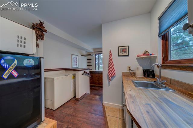 18255 Stoneview Road Monument, CO 80132 - Photo 29 of 42 Downstairs Kitchen featuring counter space, fridge, dark hardwood / wood-style flooring, black fridge, and sink. Freezer and small fridge do not stay. View to bar area in the back
