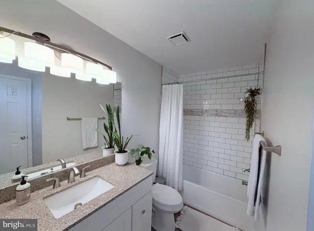 a bathroom with a granite countertop sink a mirror a shower and a toilet