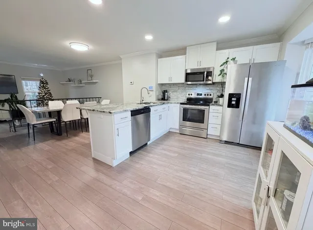 a open kitchen with stainless steel appliances granite countertop a stove top oven a sink dishwasher a refrigerator and a dining table with wooden floor