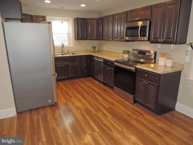 a kitchen with stainless steel appliances granite countertop a refrigerator a sink dishwasher and wooden cabinets with wooden floor