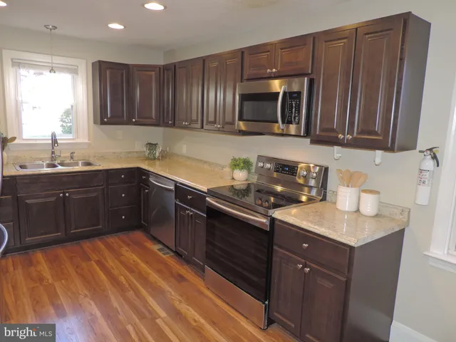 a kitchen with stainless steel appliances granite countertop wooden cabinets a stove top oven a sink and dishwasher with wooden floor