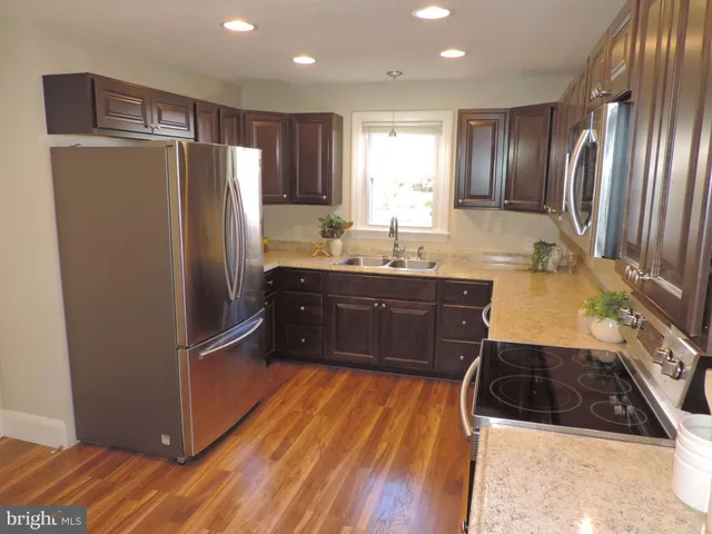 a kitchen with stainless steel appliances granite countertop a refrigerator a sink a stove and white cabinets with wooden floor