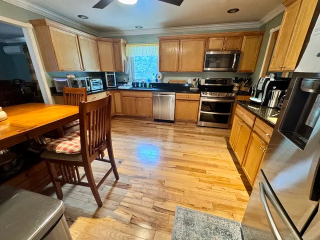 a kitchen with stainless steel appliances kitchen island granite countertop a stove top oven a sink a dining table and chairs with wooden floor