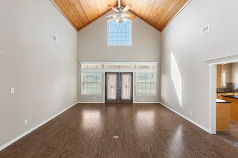an empty room with wooden floor chandelier and windows