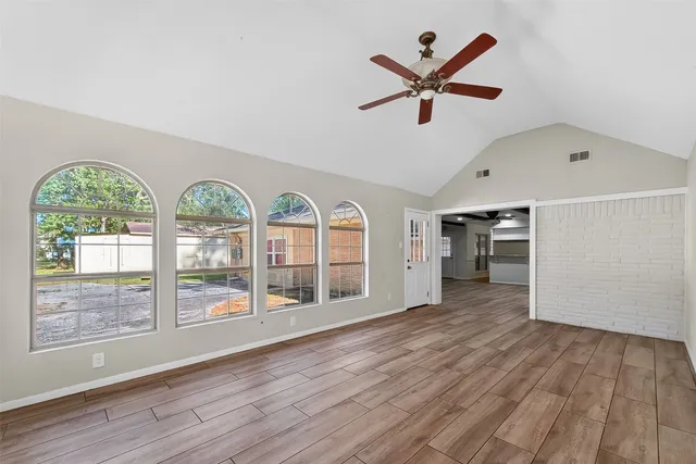 an empty room with wooden floor a ceiling fan and windows