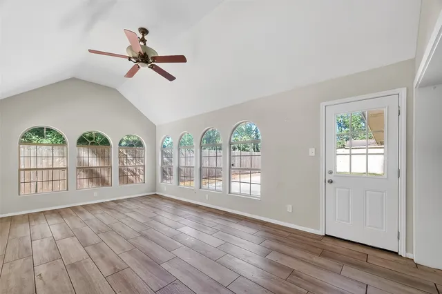an empty room with wooden floor fan and windows