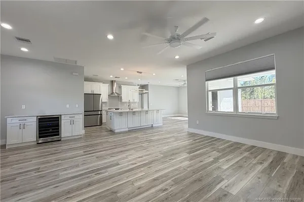 an empty room with wooden floor kitchen view and windows