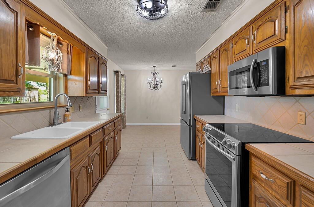 2857 Country Spring Road Lorena, TX 76655 - Photo 12 of 40 Kitchen with tile countertops, stainless steel appliances, decorative backsplash, wood finish cabinets, and a textured ceiling