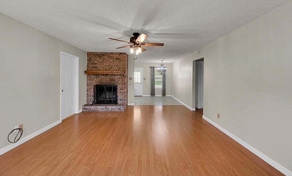 2857 Country Spring Road Lorena, TX 76655 - Photo 4 of 40 Unfurnished living room with light wood-type flooring, a ceiling fan, a textured ceiling, a brick fireplace, and suspended lighting