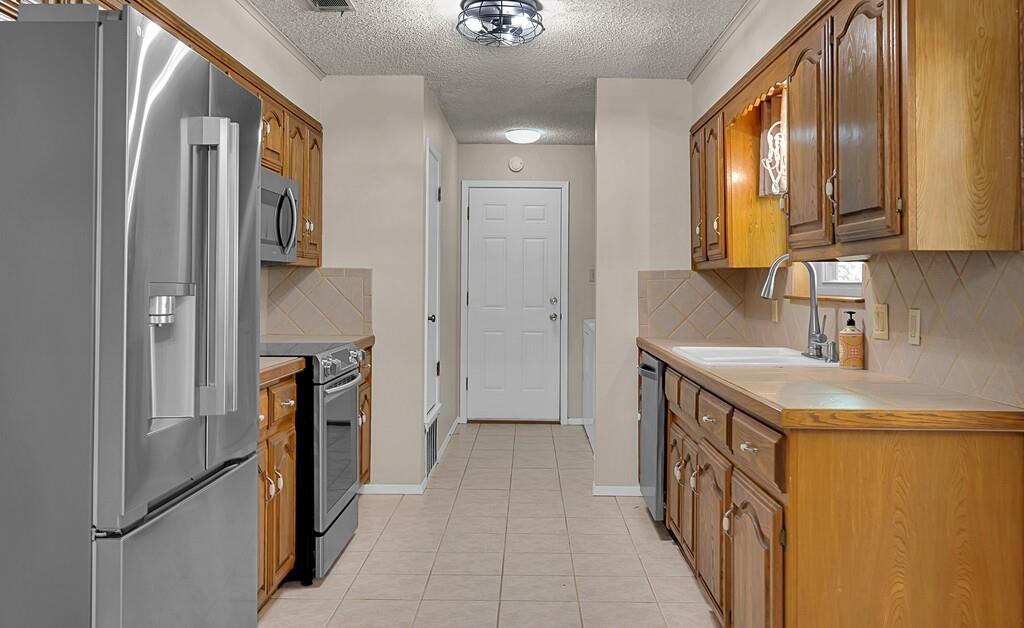 2857 Country Spring Road Lorena, TX 76655 - Photo 7 of 40 Kitchen with stainless steel appliances, backsplash, a textured ceiling, light tile patterned floors, and wood finish cabinets
