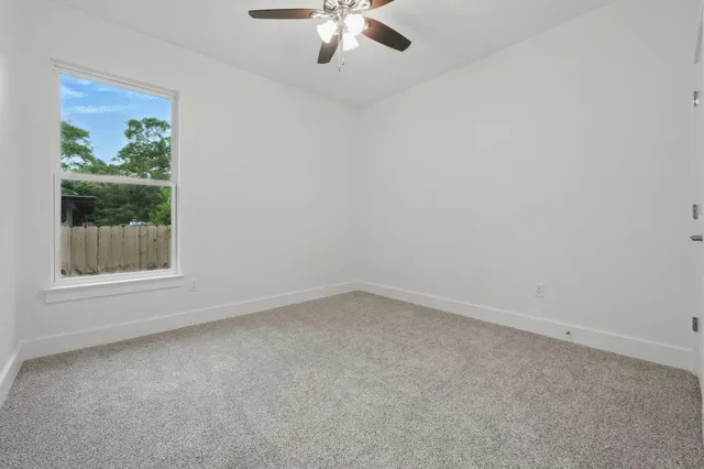 an empty room with ceiling fan and windows