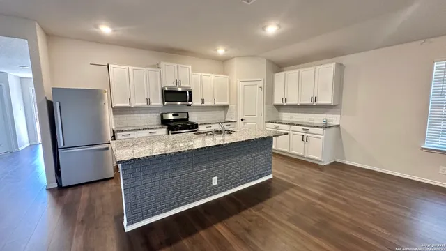 a kitchen with stainless steel appliances granite countertop a refrigerator a sink dishwasher a stove and white countertops with wooden floor