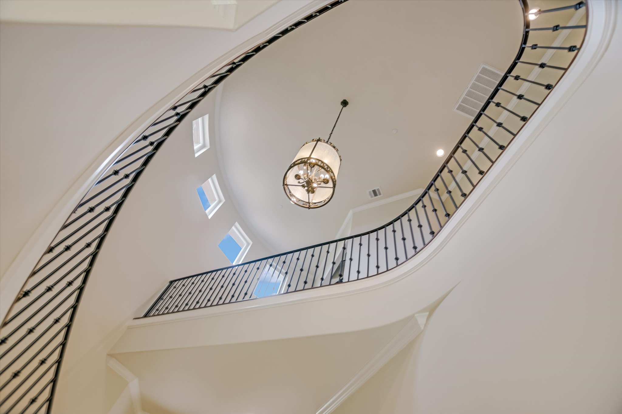 11 Inwood Circle Austin, TX 78746 - Photo 6 of 38 Dramatic curving staircase with wrought iron railings ascends beneath a grand chandelier, illuminated by strategically placed skylights.