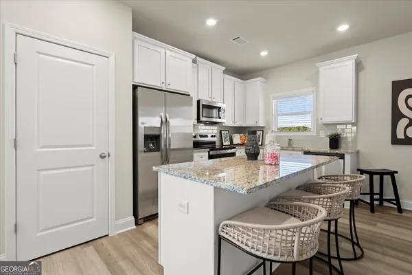 a kitchen with stainless steel appliances granite countertop a stove a refrigerator a sink a dining table and chairs