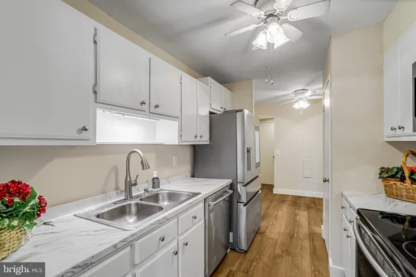 a kitchen with stainless steel appliances a sink a stove oven a refrigerator with white cabinets and wooden floor