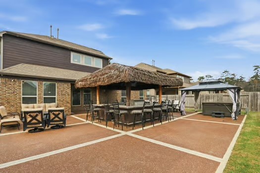 24714 Longwood Forest Drive Spring, TX 77373 - Photo 16 of 21 Spacious backyard featuring a large patio with a thatched-roof bar area, ample seating, and a gazebo-covered hot tub, perfect for entertaining and relaxation.