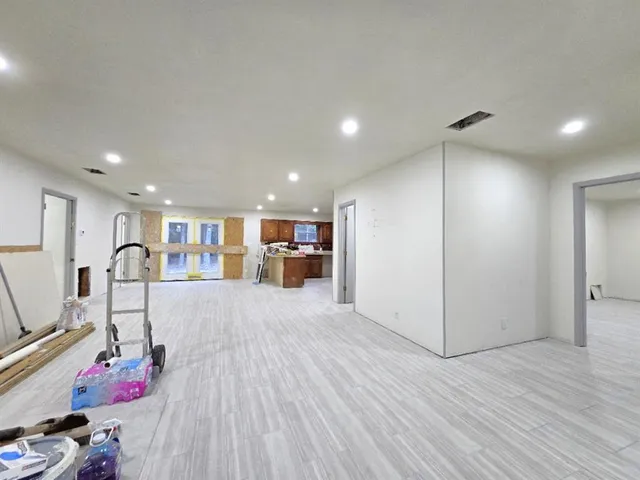 a view of an empty room with wooden floor and a kitchen