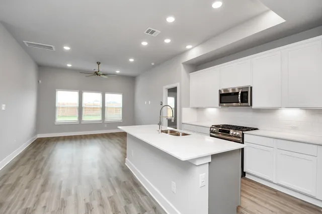 a kitchen with stainless steel appliances a stove top oven a sink dishwasher and a refrigerator with wooden floor