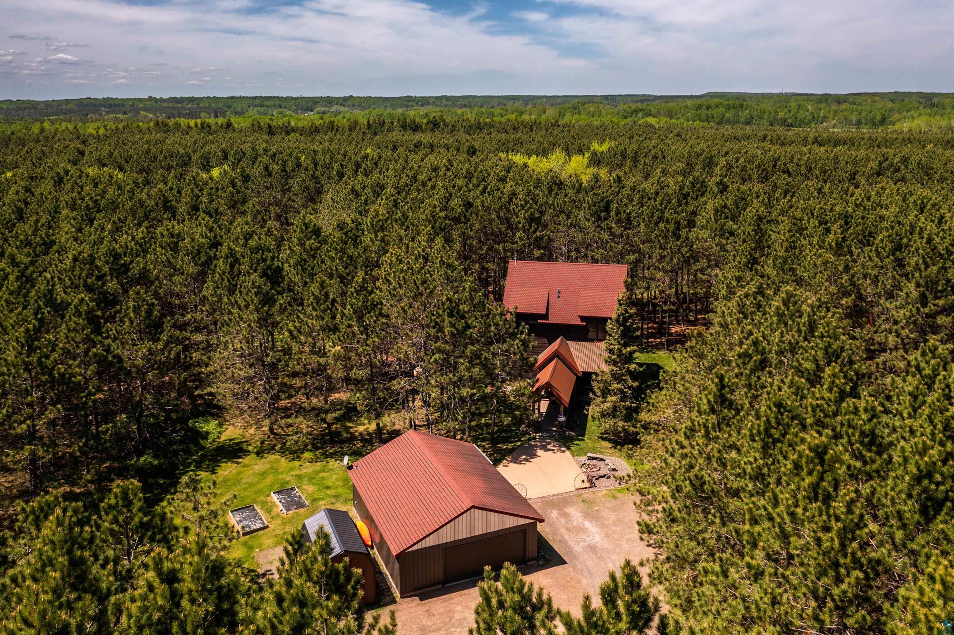 75 East Stark Road Esko, MN 55733 - Photo 77 of 87 Expansive wooded property featuring a primary residence with a red roof, a detached garage with a matching red roof, and established garden beds