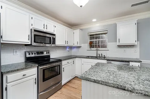 a kitchen with granite countertop white cabinets sink and stainless steel appliances