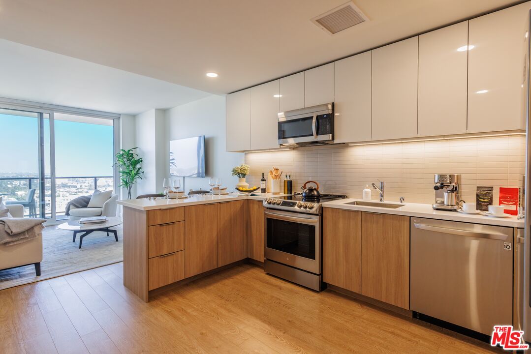 11750 Wilshire Boulevard, Unit 2404 Los Angeles, CA 90025 - Photo 6 of 38 a kitchen with stainless steel appliances granite countertop white cabinets a sink a stove a refrigerator and microwave with wooden floor