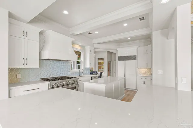 a large white living room with stainless steel appliances kitchen island granite countertop a large window and white cabinets