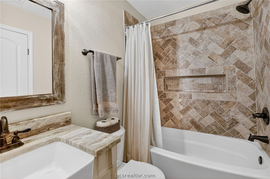 10054 Arnold Lane Bryan, TX 77845 - Photo 14 of 32 a bathroom with a granite countertop sink and a mirror a bathtub