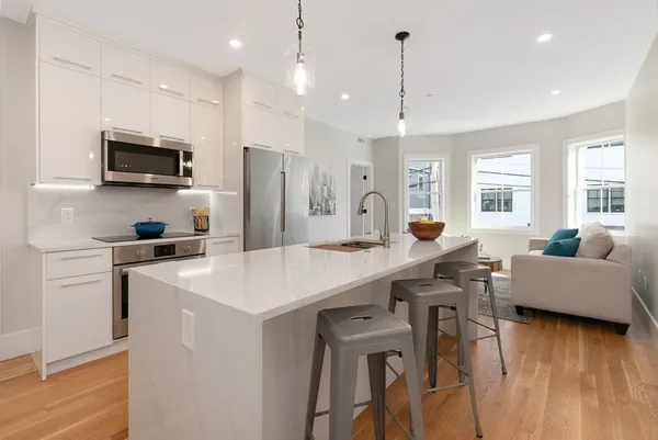 a kitchen with stainless steel appliances granite countertop a sink a stove a refrigerator and a living room with wooden floor