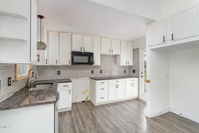 a kitchen with stainless steel appliances granite countertop a sink a stove a refrigerator and white cabinets with wooden floor