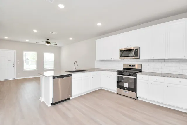 a large white kitchen with a stove a sink dishwasher and a refrigerator with wooden floor