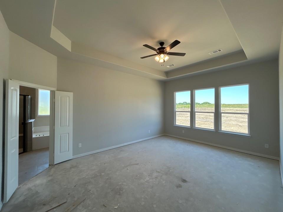 8935 County Road 623 Blue Ridge, TX 75424 - Photo 9 of 17 Spacious room with a tray ceiling, ceiling fan with light fixture, three large windows, light gray wall paint, and a double-door entry to an adjoining bathroom featuring a built-in tub