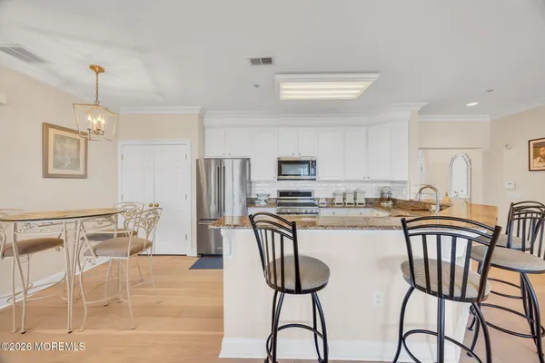 a kitchen with stainless steel appliances kitchen island granite countertop a dining table chairs and a refrigerator