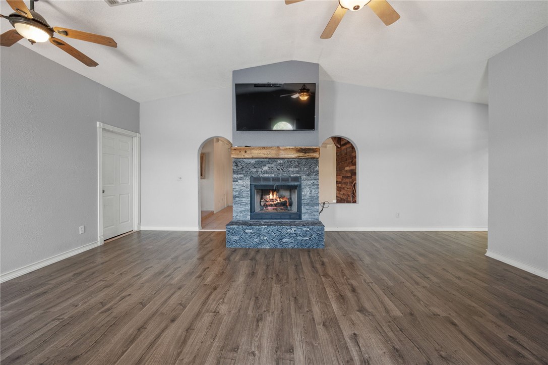 4100 North Skylark Road Kingman, AZ 86409 - Photo 41 of 60 Unfurnished living room featuring lofted ceiling, ceiling fan, dark wood-style flooring, a fireplace, and arched walkways