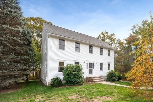 a view of a white house next to a yard with plants and trees