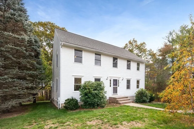 a view of a white house next to a yard with plants and trees