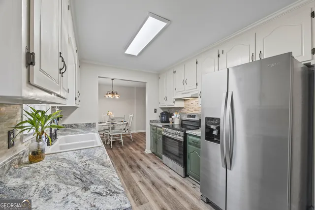 a kitchen with stainless steel appliances a refrigerator a stove a sink a dining table and chairs with wooden floor