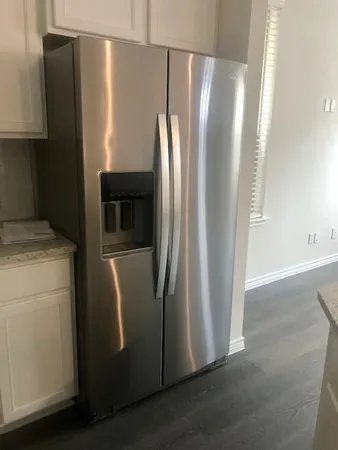 a view of a refrigerator in kitchen and an empty room with wooden floor