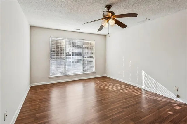 an empty room with wooden floor fan and windows