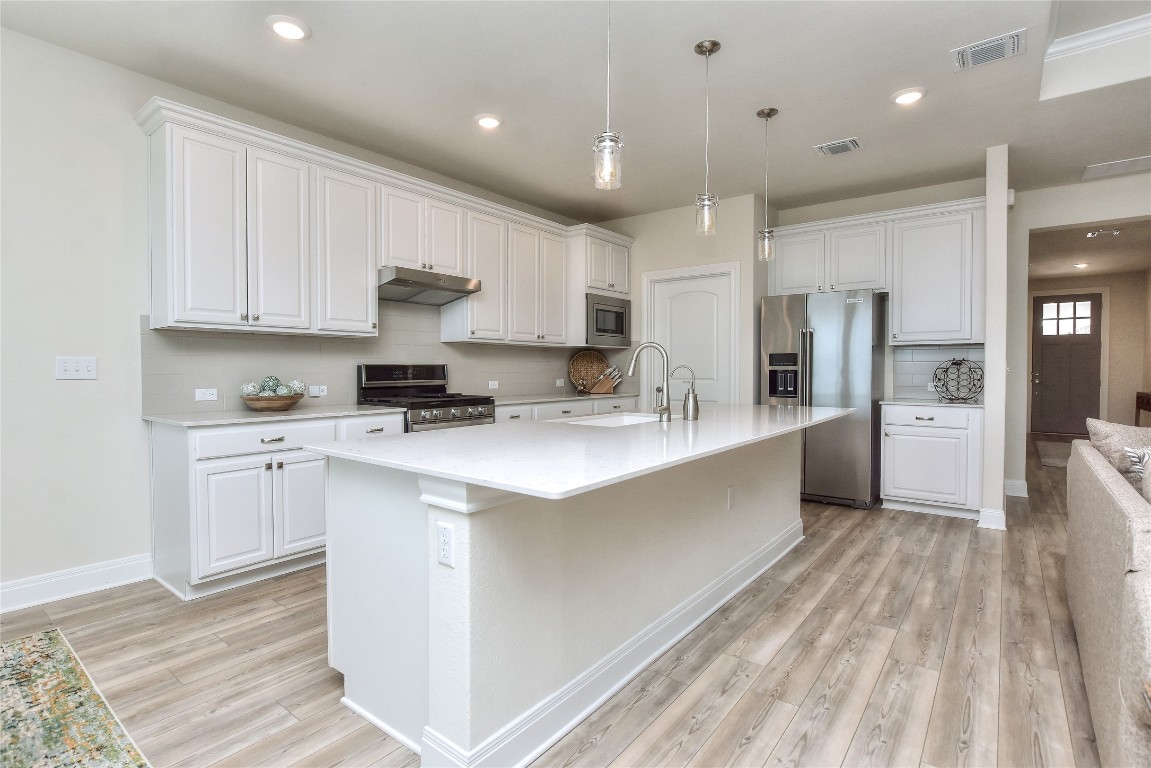 a large white kitchen with kitchen island a sink stainless steel appliances and cabinets