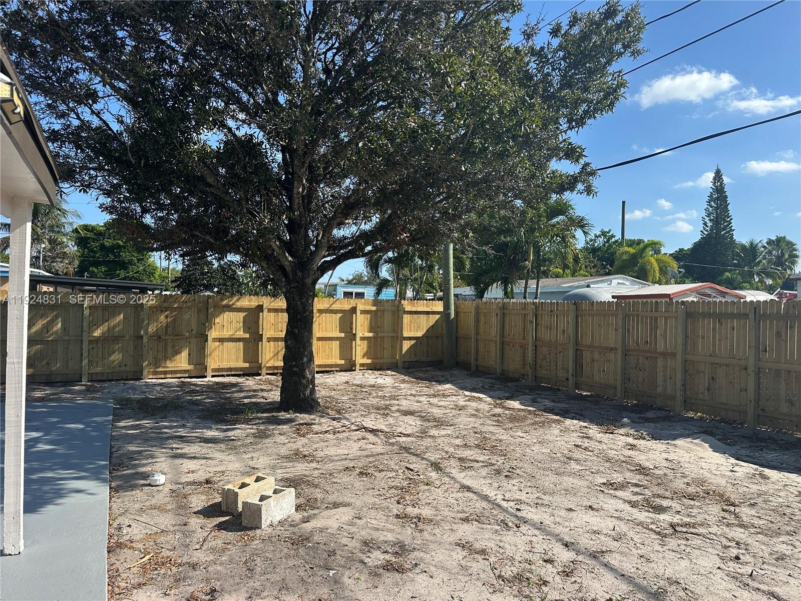 1264 Northeast 25th Court Pompano Beach, FL 33064 - Photo 19 of 19 a view of a backyard of white fence and a large tree