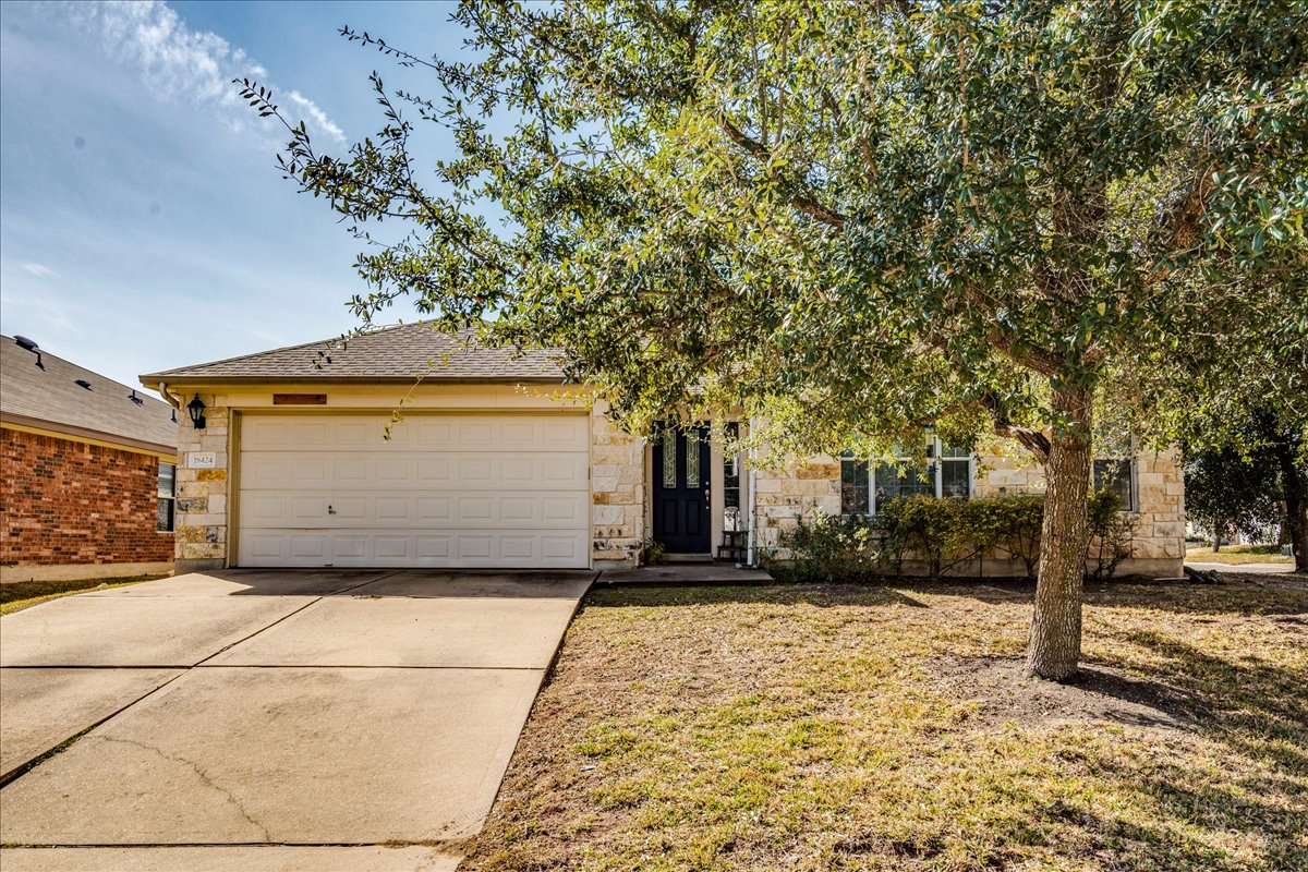 View of front facade featuring concrete driveway, stone siding, a garage, a shingled roof, and a front lawn