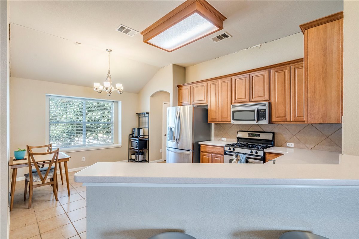 18424 Dry Brook Loop Pflugerville, TX 78660 - Photo 9 of 25 Kitchen featuring stainless steel appliances, backsplash, arched walkways, light tile patterned flooring, and a peninsula