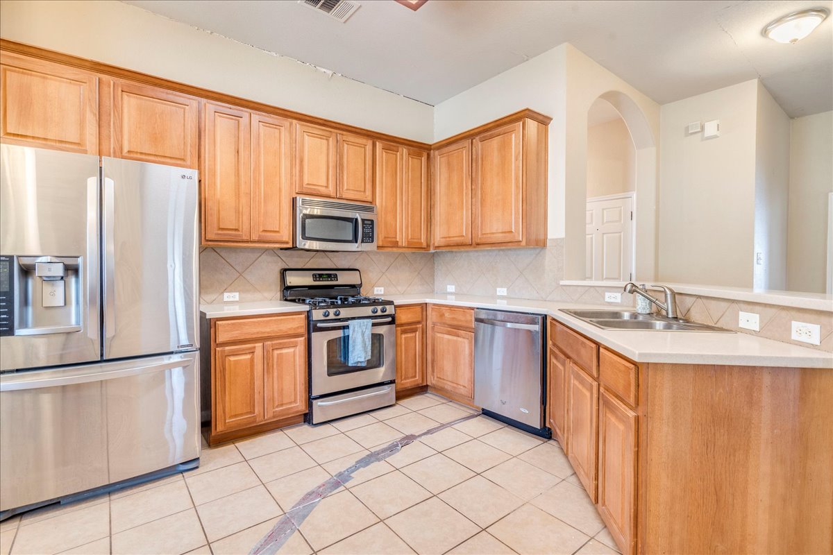 18424 Dry Brook Loop Pflugerville, TX 78660 - Photo 10 of 25 Kitchen with stainless steel appliances, a peninsula, tasteful backsplash, light tile patterned flooring, and inlaid floor details