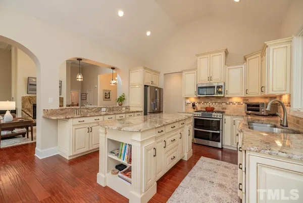 a kitchen with stainless steel appliances granite countertop a stove top oven a sink dishwasher a refrigerator and white cabinets with wooden floor