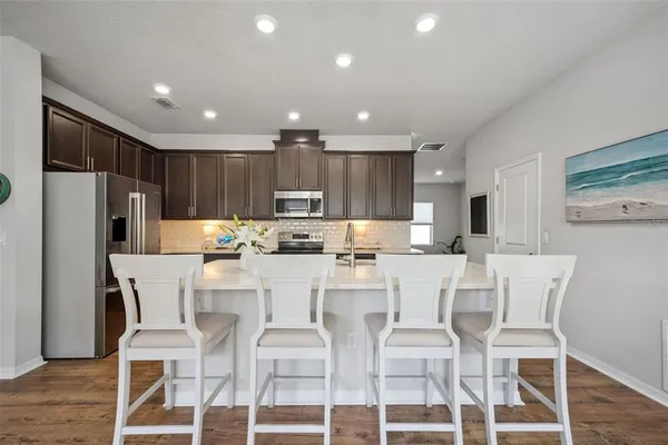 a kitchen with stainless steel appliances kitchen island granite countertop a table chairs refrigerator and microwave