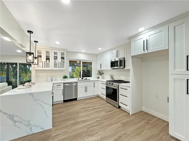 a kitchen with stainless steel appliances granite countertop a stove top oven a refrigerator a sink and dishwasher with wooden floor